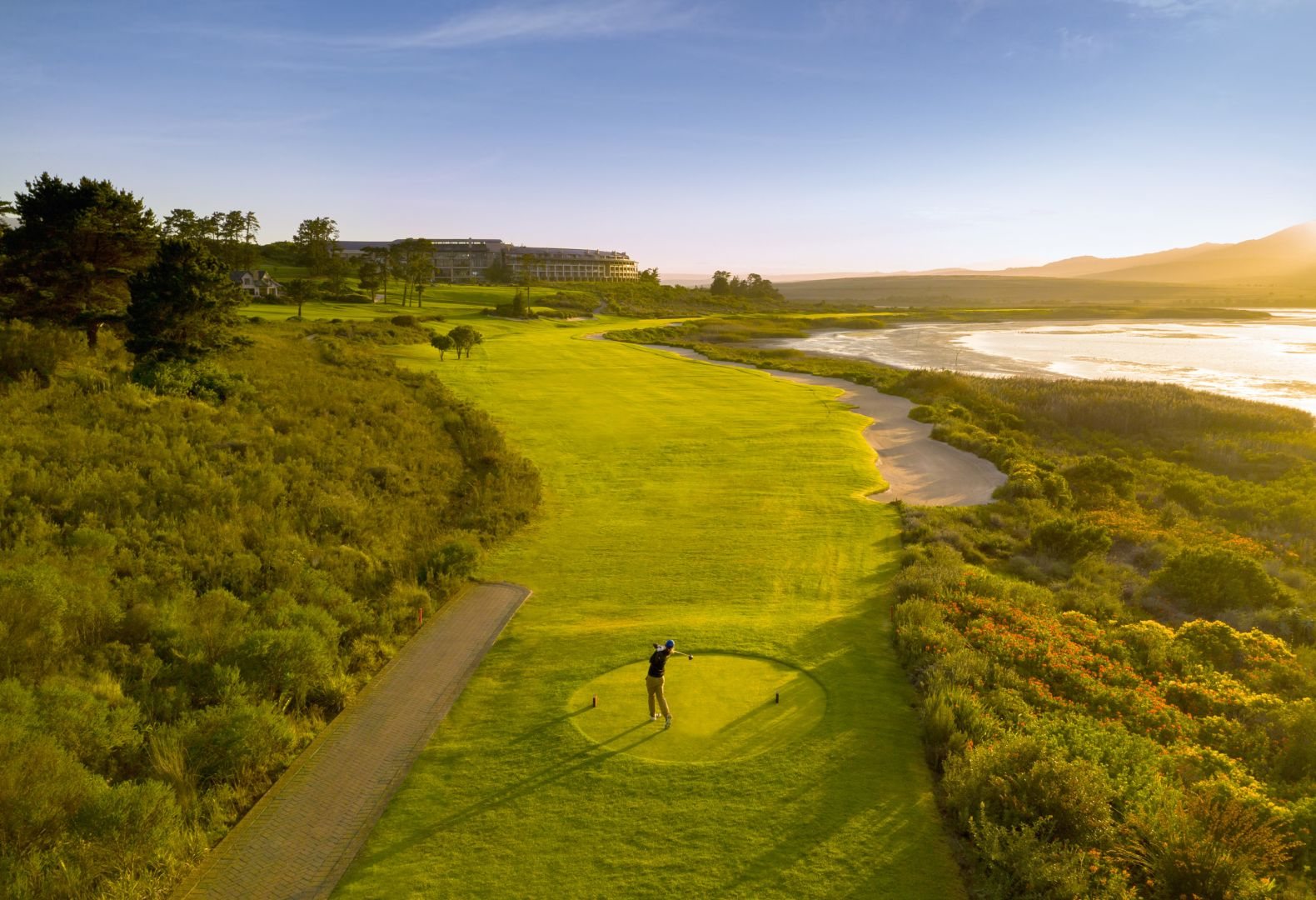 A golfer tees off beside the lagoon at Arabella in the golden evening light